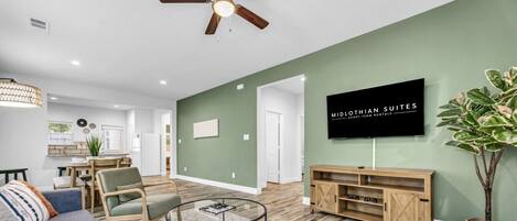 A modern living room with a flat-screen TV, a ceiling fan, and a dining area.