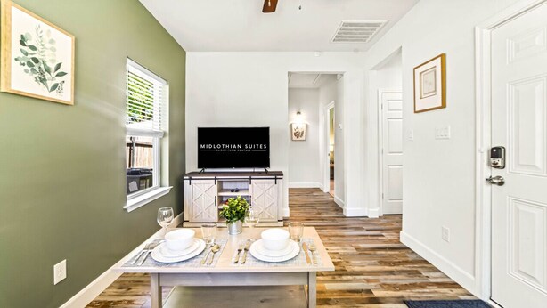 A mid-century modern styled room with a dining table set for two, a flat-screen TV, and a window with blinds. - King bed, Double unit, 2 Kitchens | TSD (Rockwall)