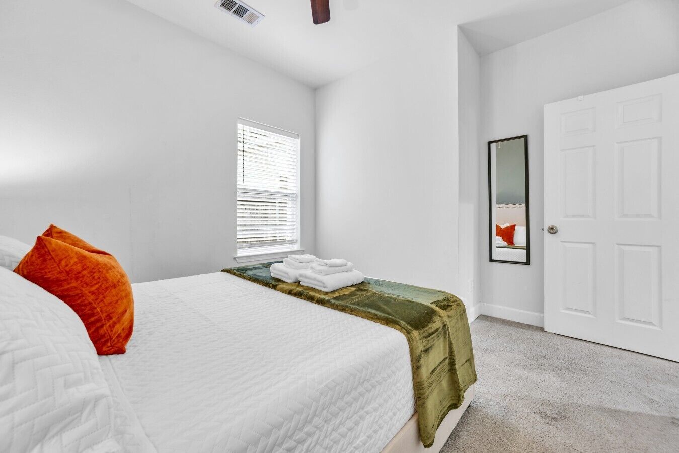 Une chambre à coucher avec un lit, une fenêtre avec des stores, une porte et un miroir sur le mur.