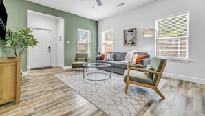 A living room with a ceiling fan, a sofa, two armchairs, a coffee table, and a door. - King bed, Double unit, 2 Kitchens | TSD (Rockwall)