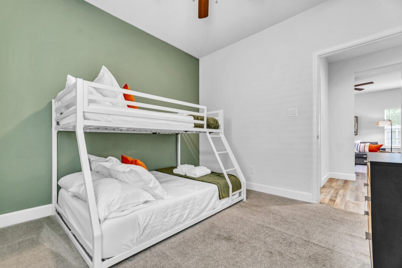 A bunk bed with white bedding, a green wall, and a carpeted floor.