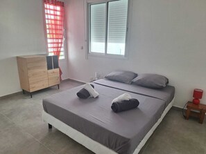 Ein Schlafzimmer mit einem Bett, einem Schminktisch, einem Fenster mit Jalousien und einem Nachttisch mit Lampe.