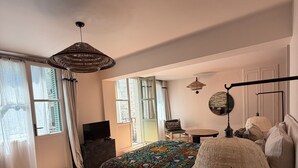 Een slaapkamer met een groot bed, een rond nachtkastje, een hanglamp en een raam met gordijnen.