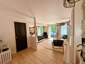 Un vaste espace de vie doté d’un plancher en bois, d’une table à manger avec des chaises, d’un canapé et d’une grande fenêtre offrant une vue sur les arbres.