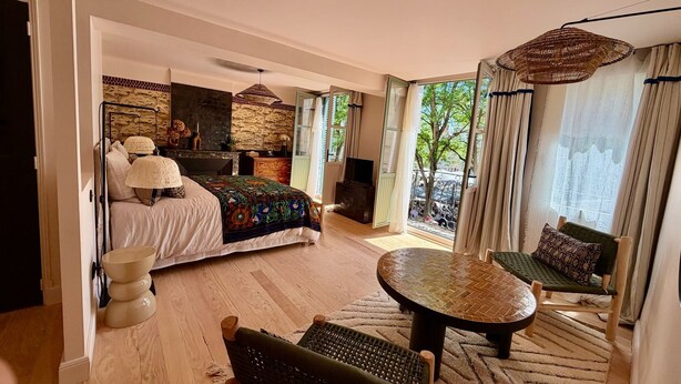 Een slaapkamer met een bed, een slaapbank, een ronde tafel en een balkon met gordijnen.