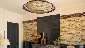Een kamer met een open haard, een bed met een kleurrijk dekbed, een houten dressoir en een hanglamp.
