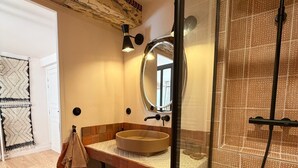 Een badkamer met een rond wastafel, een spiegel, een douche en een behang met een patroon.