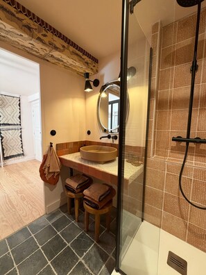 Une salle de bain avec un lavabo rond, un miroir, une douche et un mur décoré d’un motif.