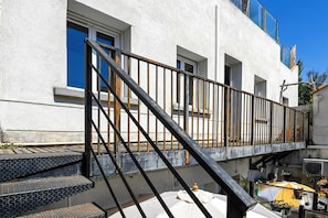 Un bâtiment doté d’un escalier, d’un balcon et d’un petit espace extérieur aménagé avec des parasols.