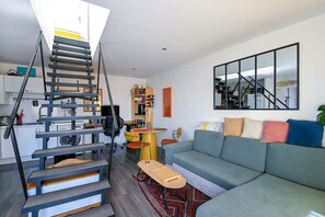 Un appartement moderne doté d’un escalier central, d’un espace de vie avec un canapé, une table à manger et un coin cuisine.