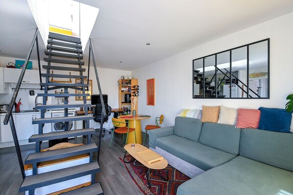 Un apartamento moderno con una escalera central, una sala de estar con sofá, una mesa de comedor y una cocina.