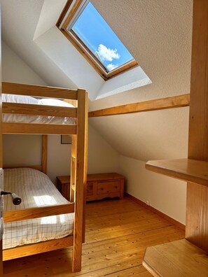 Ein Stockbett mit Dachfenster, Holzboden und einem kleinen Holzkasten.