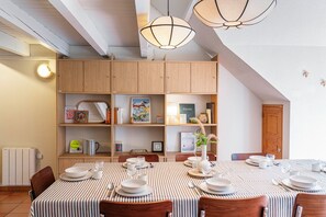 A dining area with a striped tablecloth, wooden chairs, and a bookshelf filled with books and decorative items. - Apartment - heart of the village (La Salle-les-Alpes)