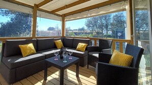 An outdoor covered patio with a sofa, chairs, and a table with wine glasses. - Chalet near the sea with garden and shared pool (Talmont-Saint-Hilaire)