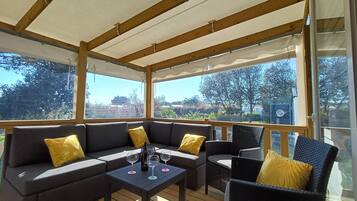Une terrasse extérieure couverte, aménagée avec un canapé, des fauteuils et une table, ainsi que des verres à vin.