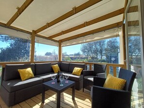 Une terrasse extérieure couverte, aménagée avec un canapé, des fauteuils et une table, ainsi que des verres à vin.