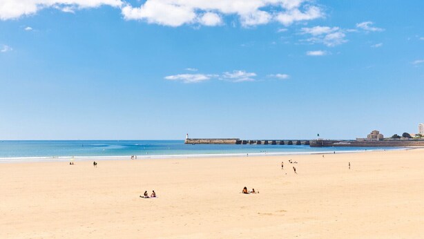 A wide sandy beach with a pier extending into the water, a clear sky, and a few people scattered across the sand. - Chalet near the sea with garden and shared pool (Talmont-Saint-Hilaire)