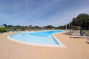 A large outdoor swimming pool with lounge chairs and a tiled deck.