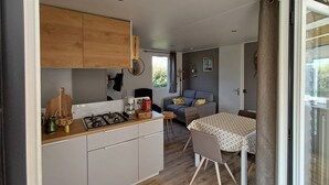 A compact kitchen with a gas stove, wooden cabinets, and a dining area with a table and chairs. - Chalet near the sea with garden and shared pool (Talmont-Saint-Hilaire)
