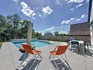 Ein Garten mit Swimmingpool, zwei orangefarbene Liegestühle, einem überdachten Patio-Tisch und einem Holzzaun.