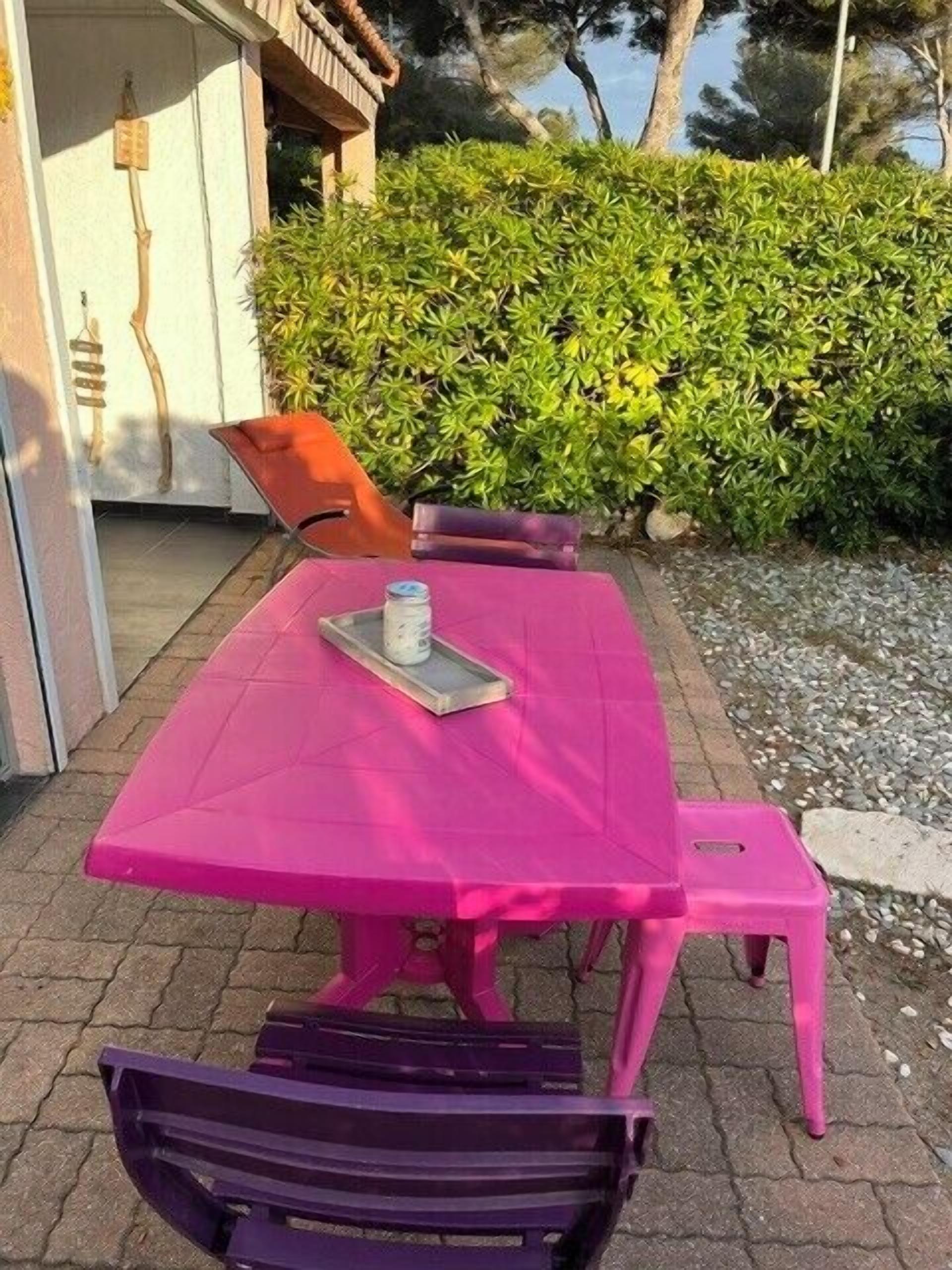Une table rose avec un plateau, deux chaises et un banc.