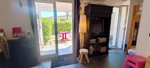 Ein Zimmer mit einer Glastür, die auf eine Terrassenförmige Außenfläche führt, einem kleinen Hocker, einem Regal mit Körben und einem rosa Sitzhocker.