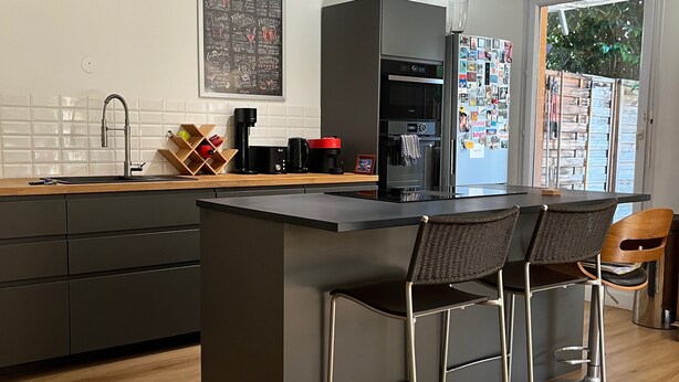 Una cocina moderna con una isla central, taburetes de bar, una cafetera y un refrigerador.