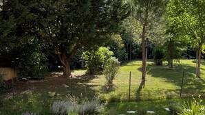 Un banco y una mesa de madera en un jardín, con vista a una zona de césped y árboles.