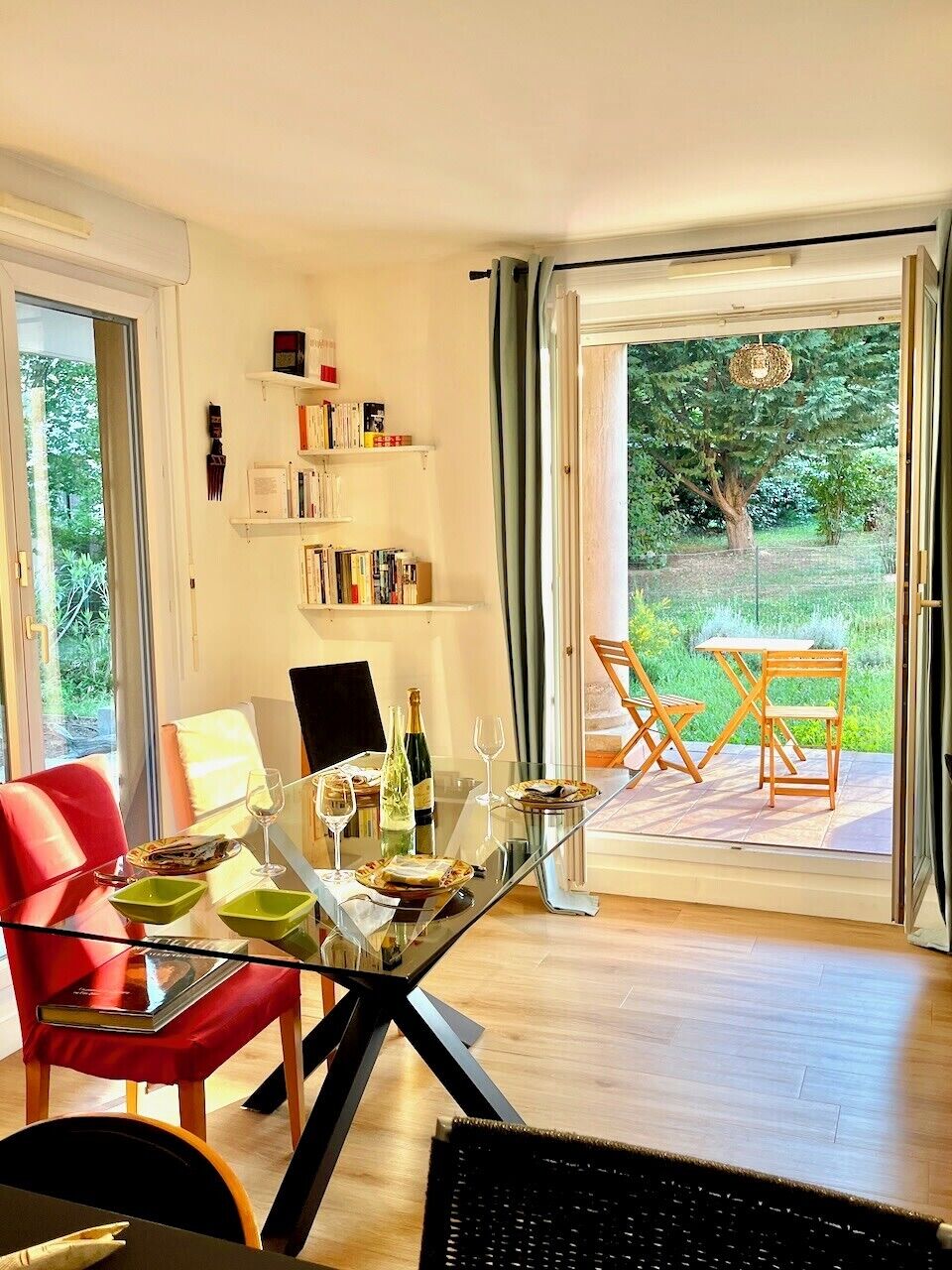 A dining area with a glass table, red chairs, and a view of a garden through a sliding glass door.