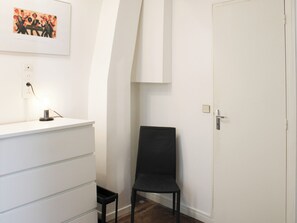 Ein Zimmer mit einem weißen Schminktisch, einem schwarzen Stuhl, einer Tür und einem gerahmten Bild an der Wand.