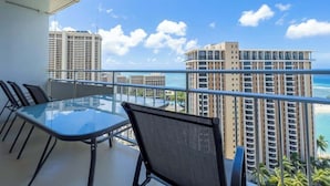 Un balcone con un tavolo e sedie in vetro, vista sulla spiaggia e grattacieli.