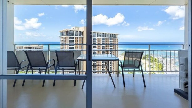 Un balcón con mesa y sillas, con vista a una playa y un edificio.