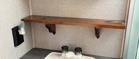 A bathroom with a white sink, wooden shelf, and a mirror above it.