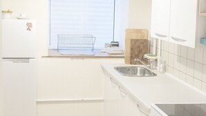 A kitchen with white cabinets, a window with blinds, a wooden cutting board, a sink, and a stove. - Java inspired Flat near Central St. (Aalborg)