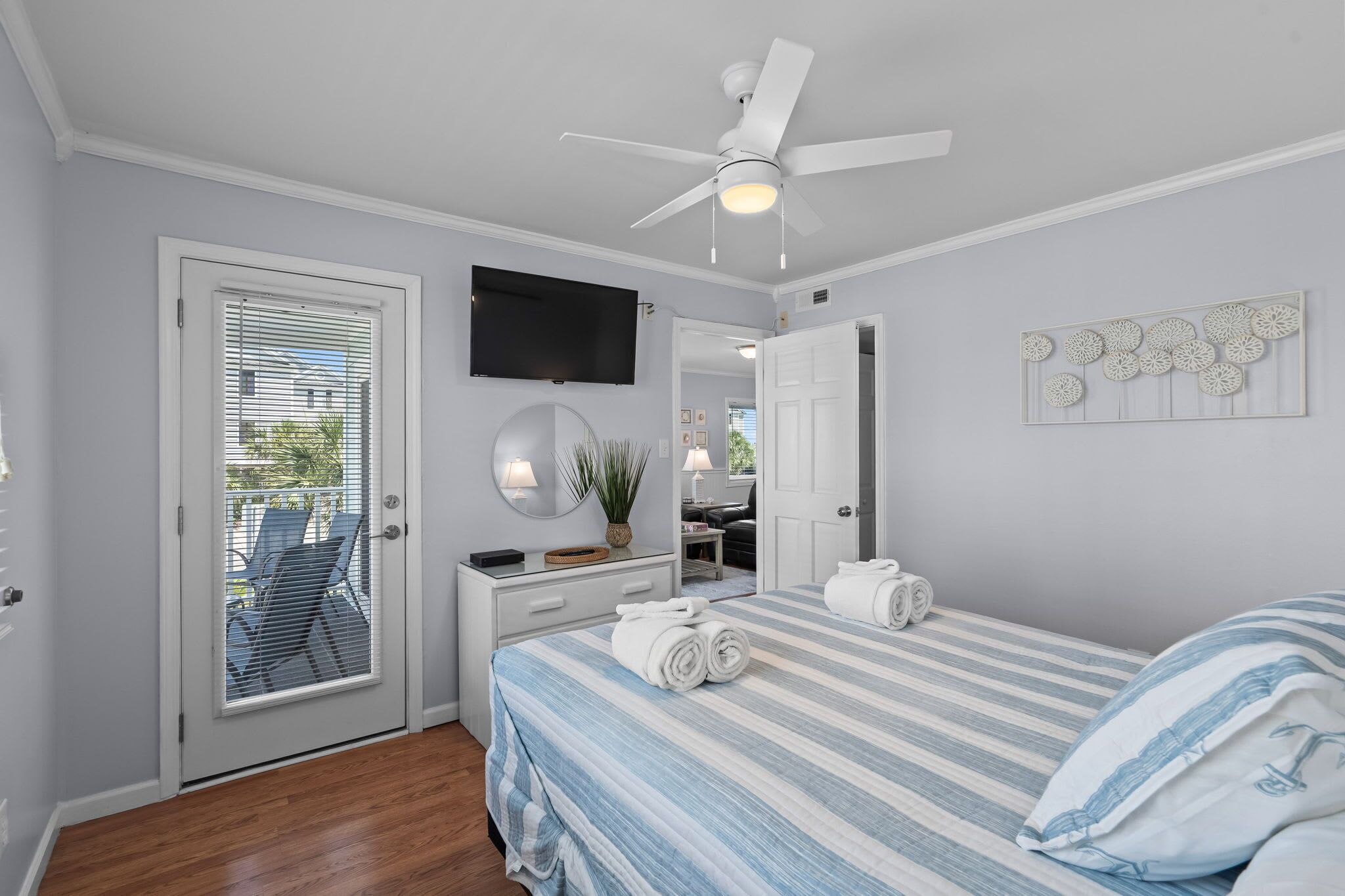 A bedroom with a bed, a ceiling fan, a TV, a mirror, and a door leading to a balcony.