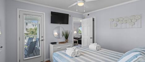A bedroom with a bed, a ceiling fan, a TV, a mirror, and a door leading to a balcony.