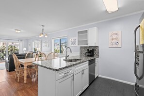 A modern kitchen with white cabinets, a granite countertop, and a built-in dishwasher. - Coastal Retreat Ocean and Pool Views 1st Floor (Murrells Inlet)