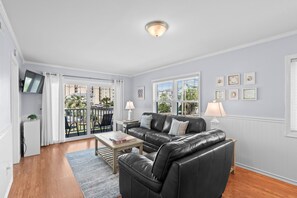 A living room with a black leather sofa, a wooden coffee table, and a TV mounted on the wall. - Coastal Retreat Ocean and Pool Views 1st Floor (Murrells Inlet)