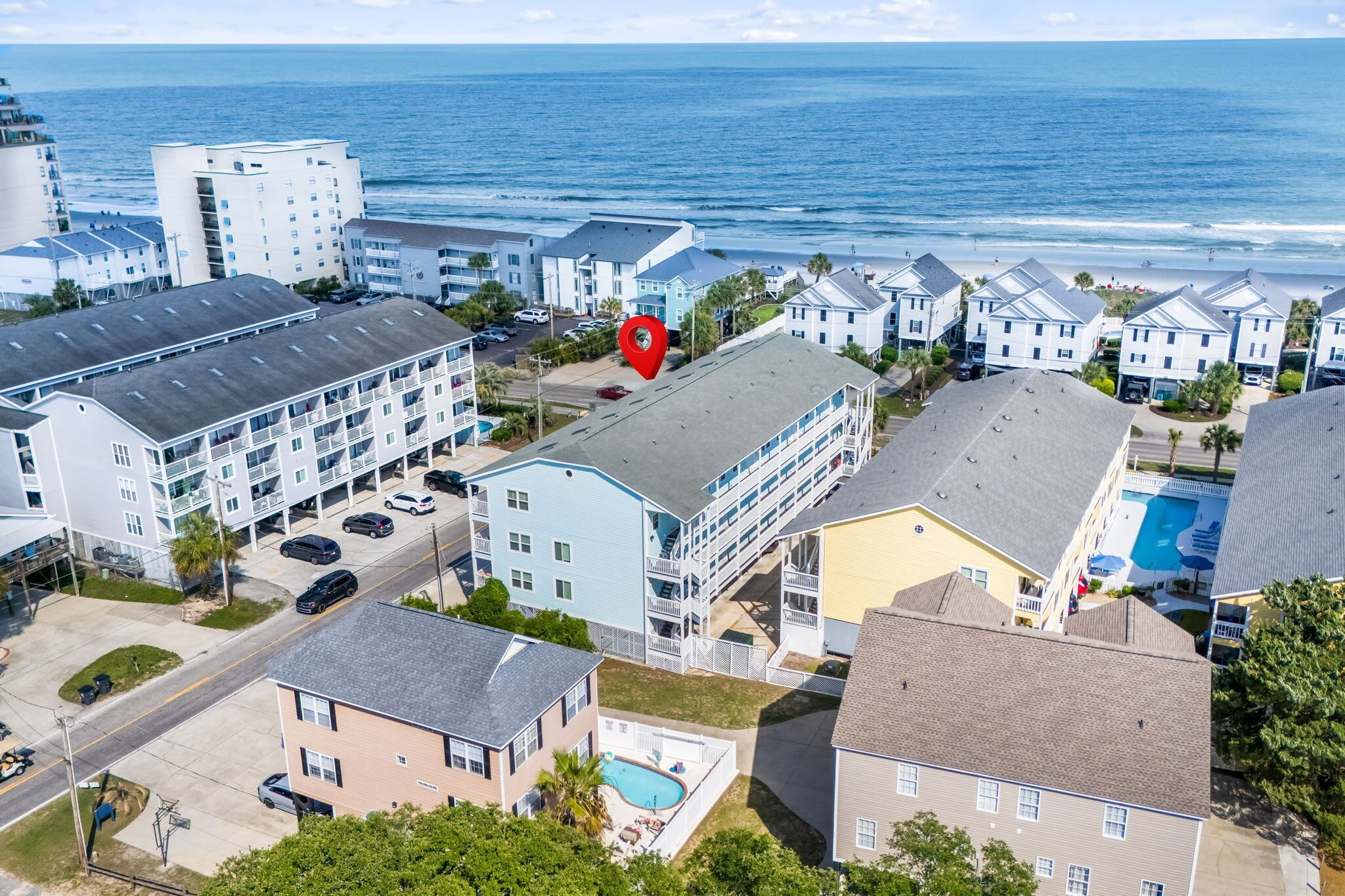 Uma área residencial costeira com vários edifícios de apartamentos, uma piscina e vista para o oceano.