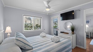 Une chambre à coucher avec un lit, un ventilateur de plafond, une télévision, une fenêtre et une table de chevet.