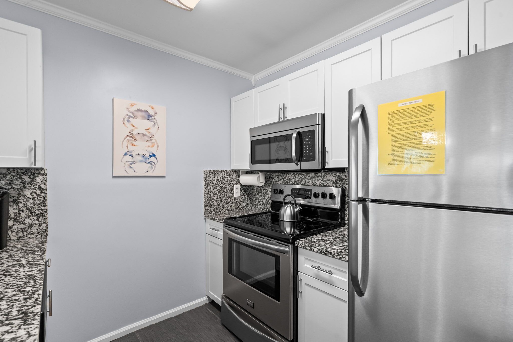 A kitchen with white cabinets, stainless steel appliances, a granite countertop, and a wall-mounted artwork.
