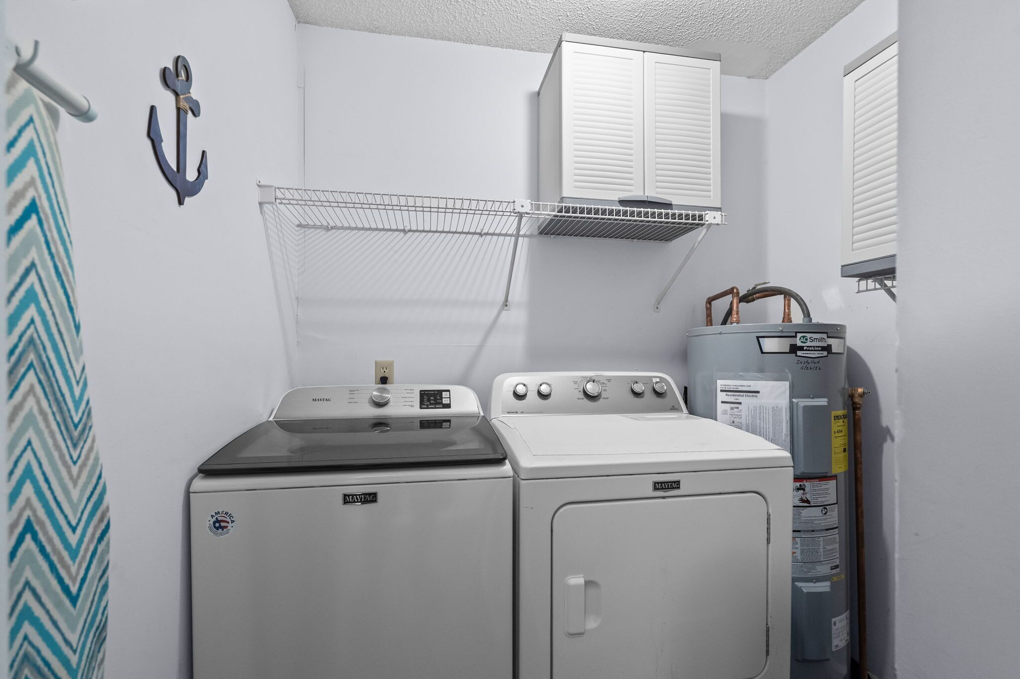 Una sala de lavandería con lavadora y secadora Maytag, un tendedero y un calentador de agua.