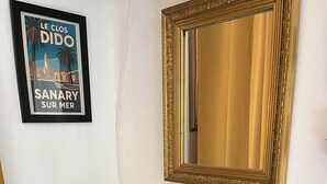 A hotel room with a framed poster, a mirror, a tray with mugs, a coffee maker, and a small table with a picture frame and a vase. - Fully-equipped room, pets welcome, 13-minute walk to the sea. (Sanary-sur-Mer)