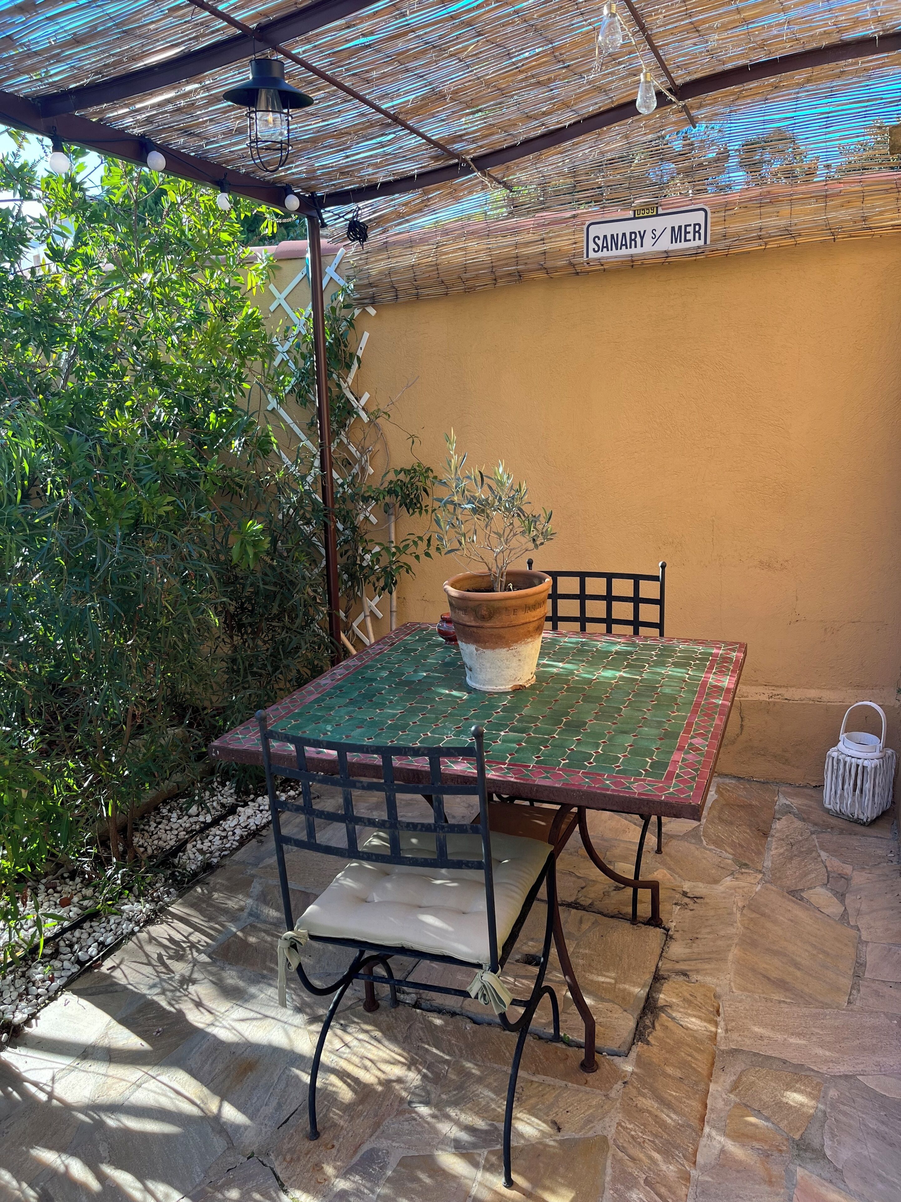 Un patio con una mesa y sillas, una planta en maceta y un letrero que dice 'SANARY S/MER'.