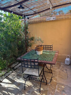 En terrasse med et bord, stole, en potteplante og et skilt med teksten 'SANARY S/MER'.