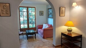 Una sala de estar con un sofá, una mesa de centro, una lámpara y vistas a otra habitación a través de un arco.