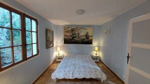 Un dormitorio con una cama, dos lámparas de noche, un cuadro y una ventana con vistas a árboles.