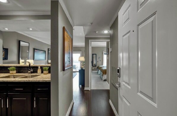 A hallway with a kitchen area, a bed, and a door leading to another room.