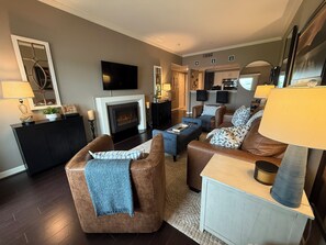 A living room with a fireplace, a television, and a kitchen area in the background.