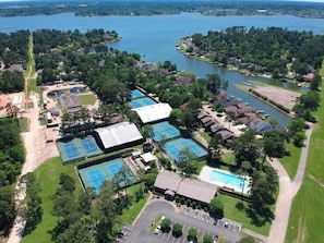 An aerial view of a lakeside property with multiple tennis courts, a swimming pool, and a parking area.